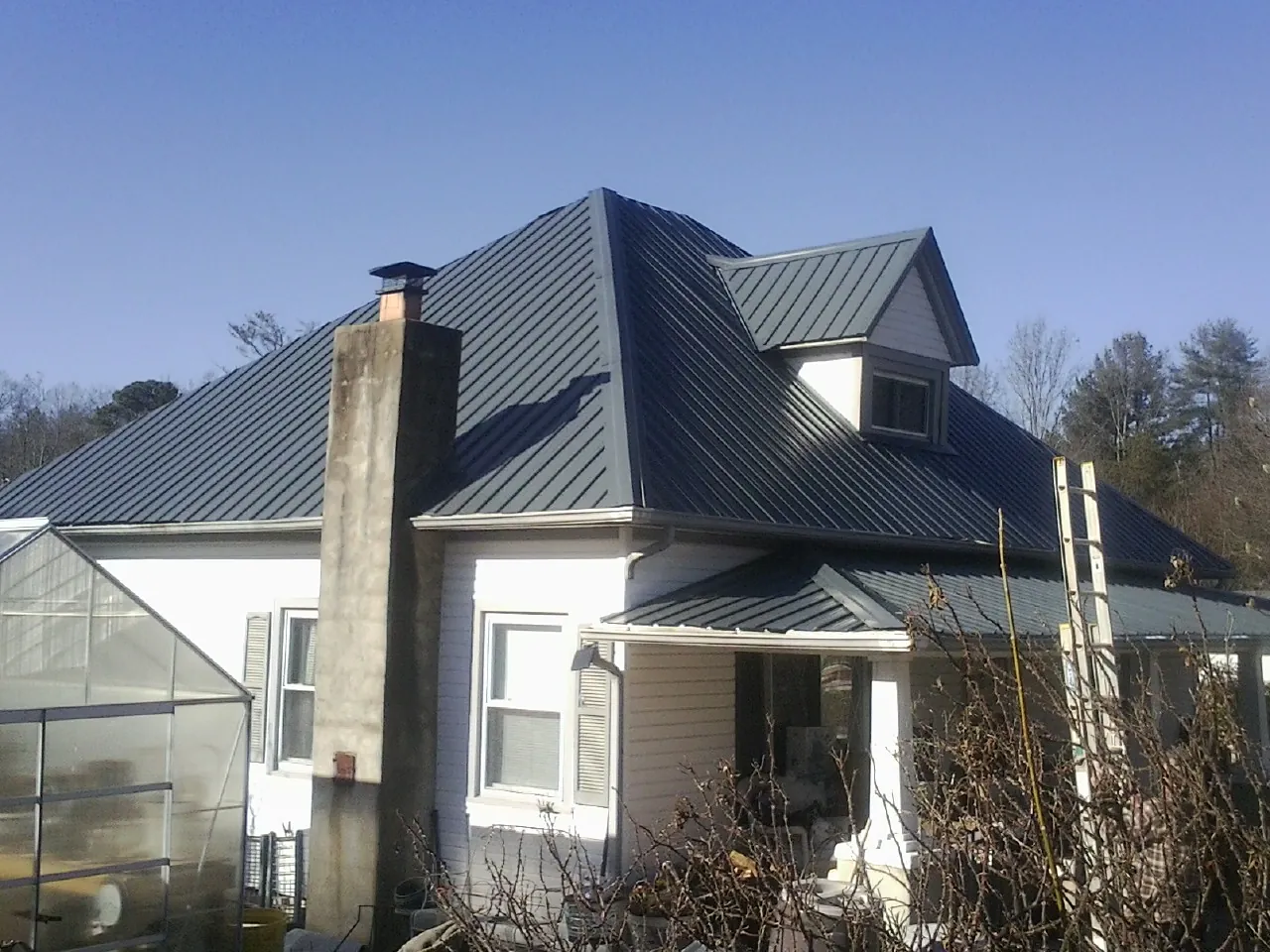 Dark blue standing seam metal roof on a white farmhouse with dormer — Slate & Tile Roof Repair by Roofing Brothers in Braddyville