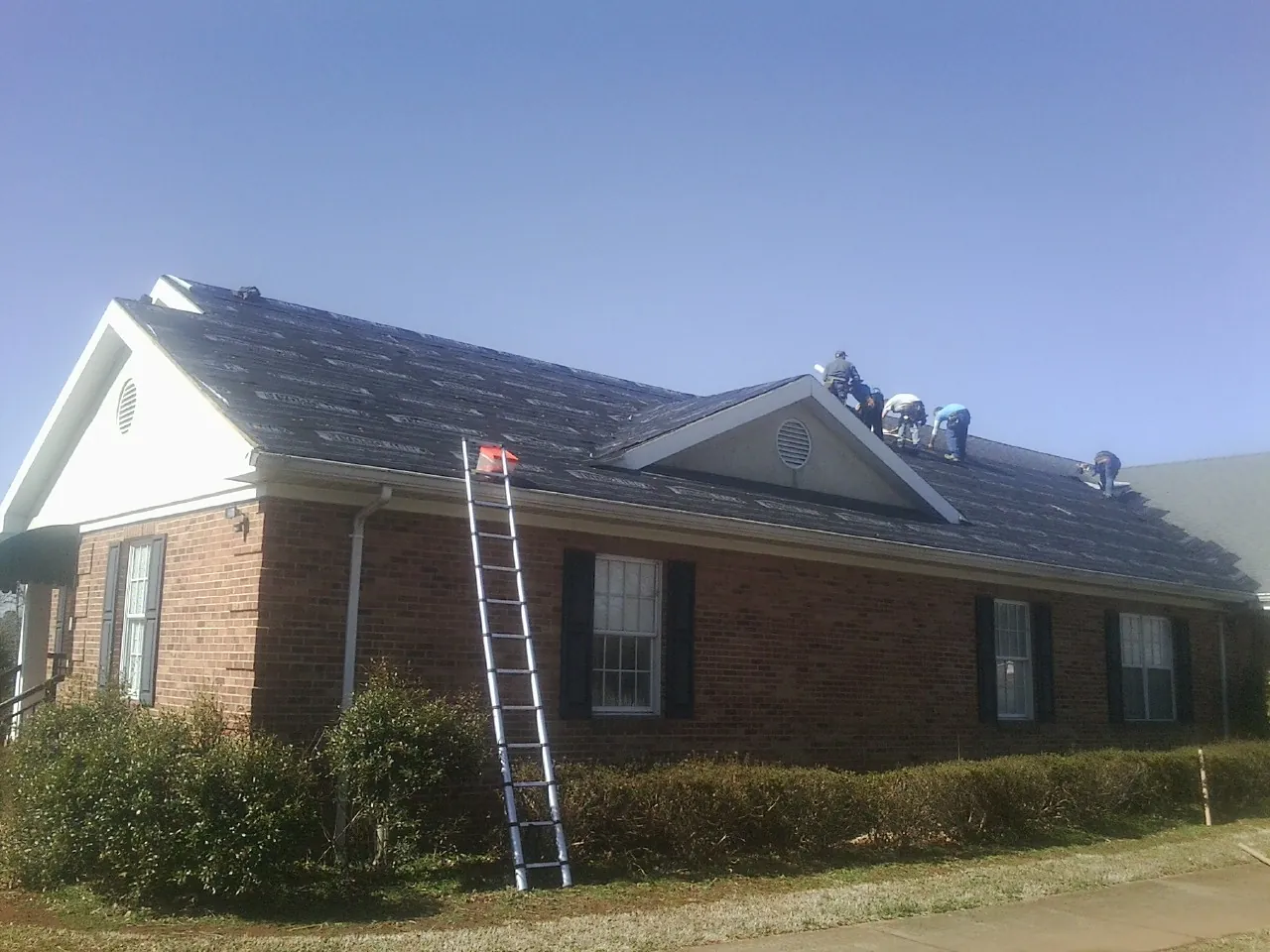 Crew tearing shingles off a brick ranch roof with a ladder set — Emergency Roof Repair work by our crew in Braddyville