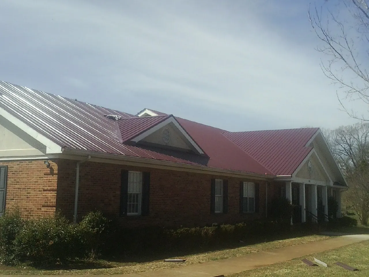 Red metal roof with gabled entries on a long brick building, from a Hail Damage Roof Repair job in Braddyville