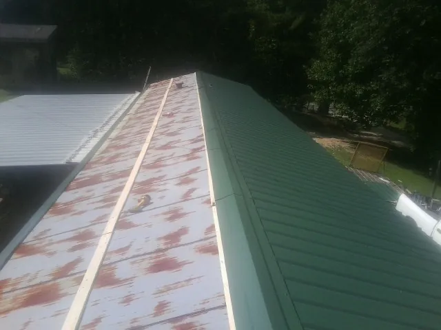 Old rusted panels beside newly installed green metal roofing — Wind Damage Roof Repair by Roofing Brothers in Braddyville