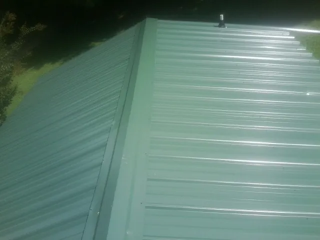 New green metal panels meeting at the ridge of a roof — Flat Roof Repair work by our crew in Braddyville