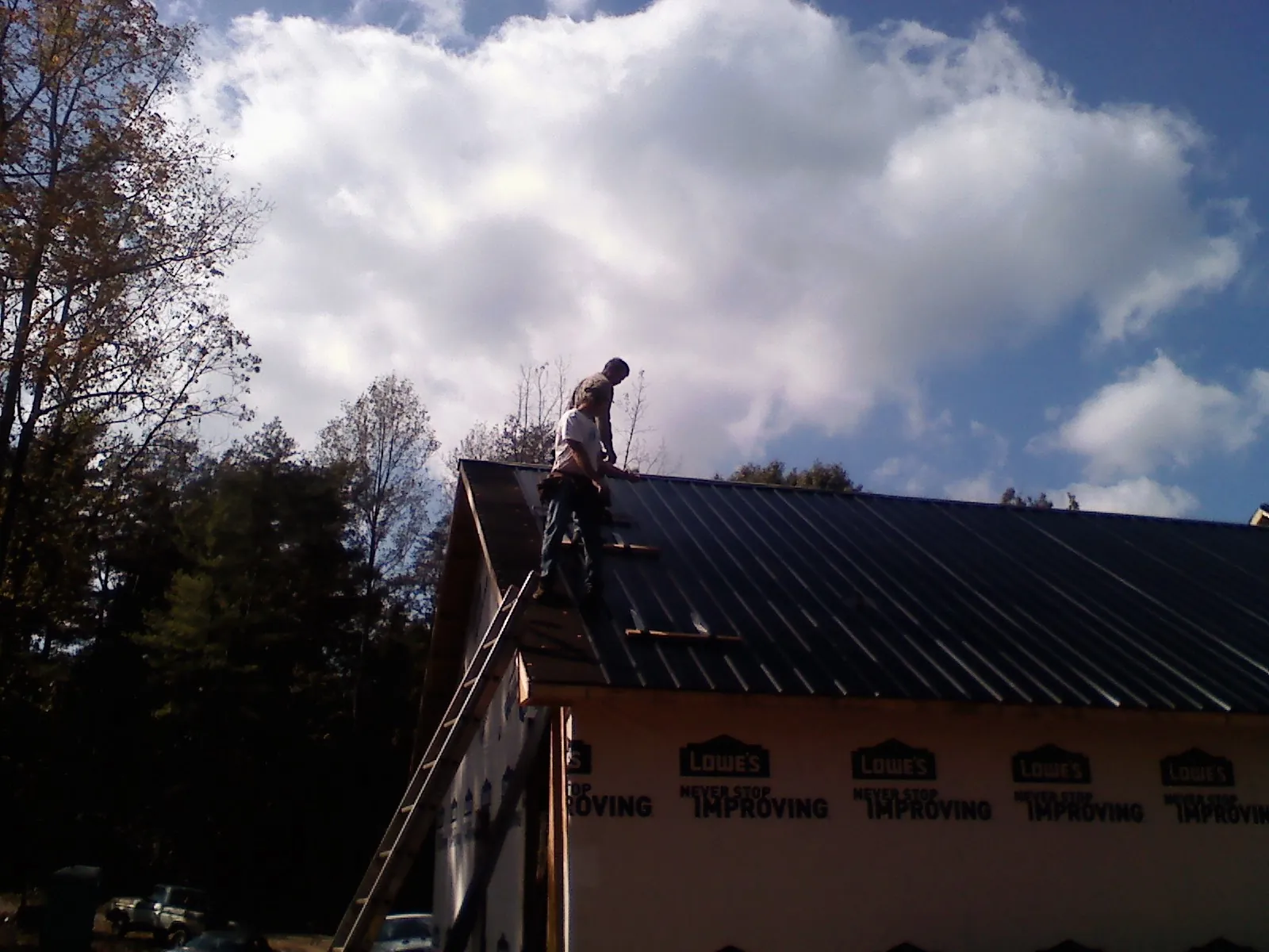 Roofer fastening dark metal panels high against a cloudy sky, from a Roof Inspection job in Braddyville