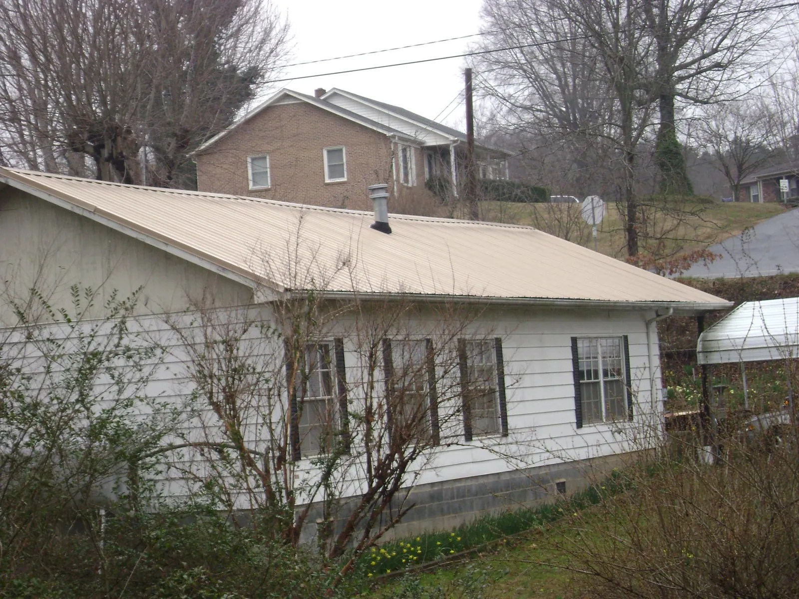 Tan metal roof on a white sided house set into a hillside — Commercial Roofing by Roofing Brothers in Braddyville
