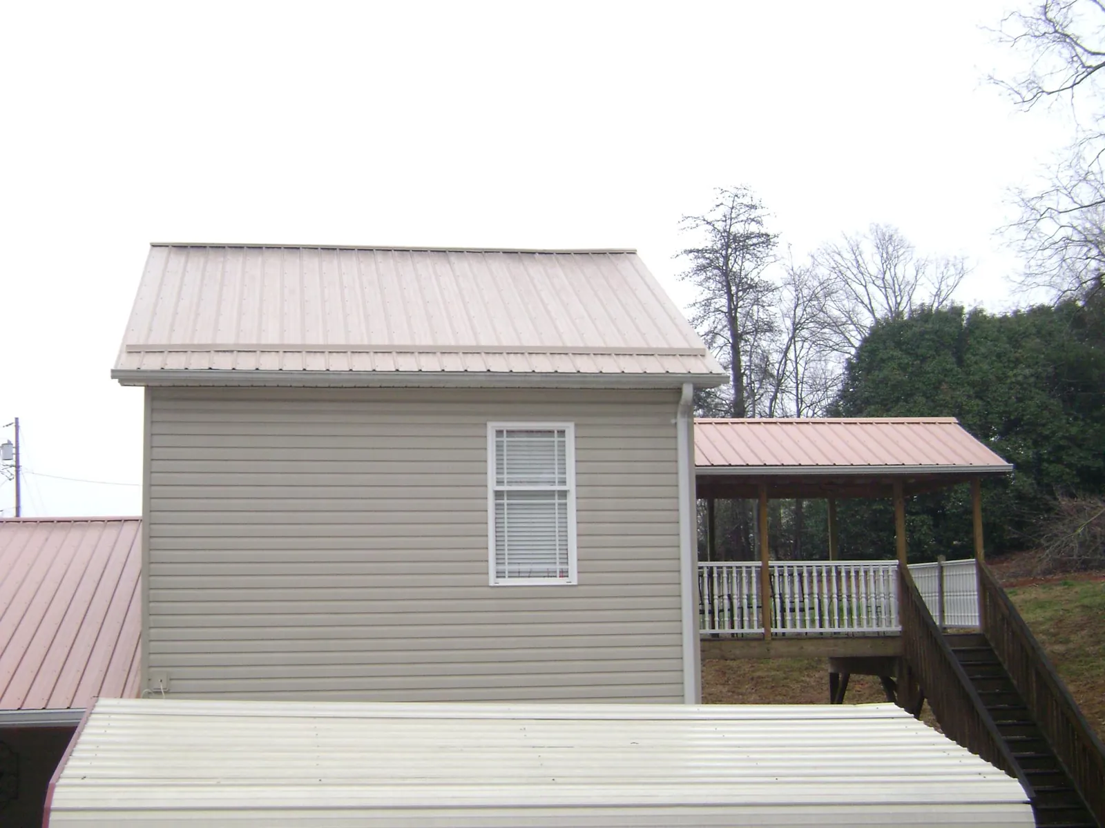 Tan metal roofs on a two story addition and attached porch, from a Roof Replacement job in Braddyville